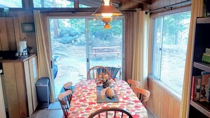 A wooden cabin dining area with a table set for four, a hanging light fixture, and a view of the outdoors through large windows. - Bobcat`s Casita- Primal Serene Surroundings, Nearby Lake Estes, 9 and 18 hole golf, Stanley Hotel! (Estes Park)