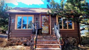 A small cabin with a stone foundation, wooden exterior, and a welcoming front door. - Bobcat`s Casita- Primal Serene Surroundings, Nearby Lake Estes, 9 and 18 hole golf, Stanley Hotel! (Estes Park)
