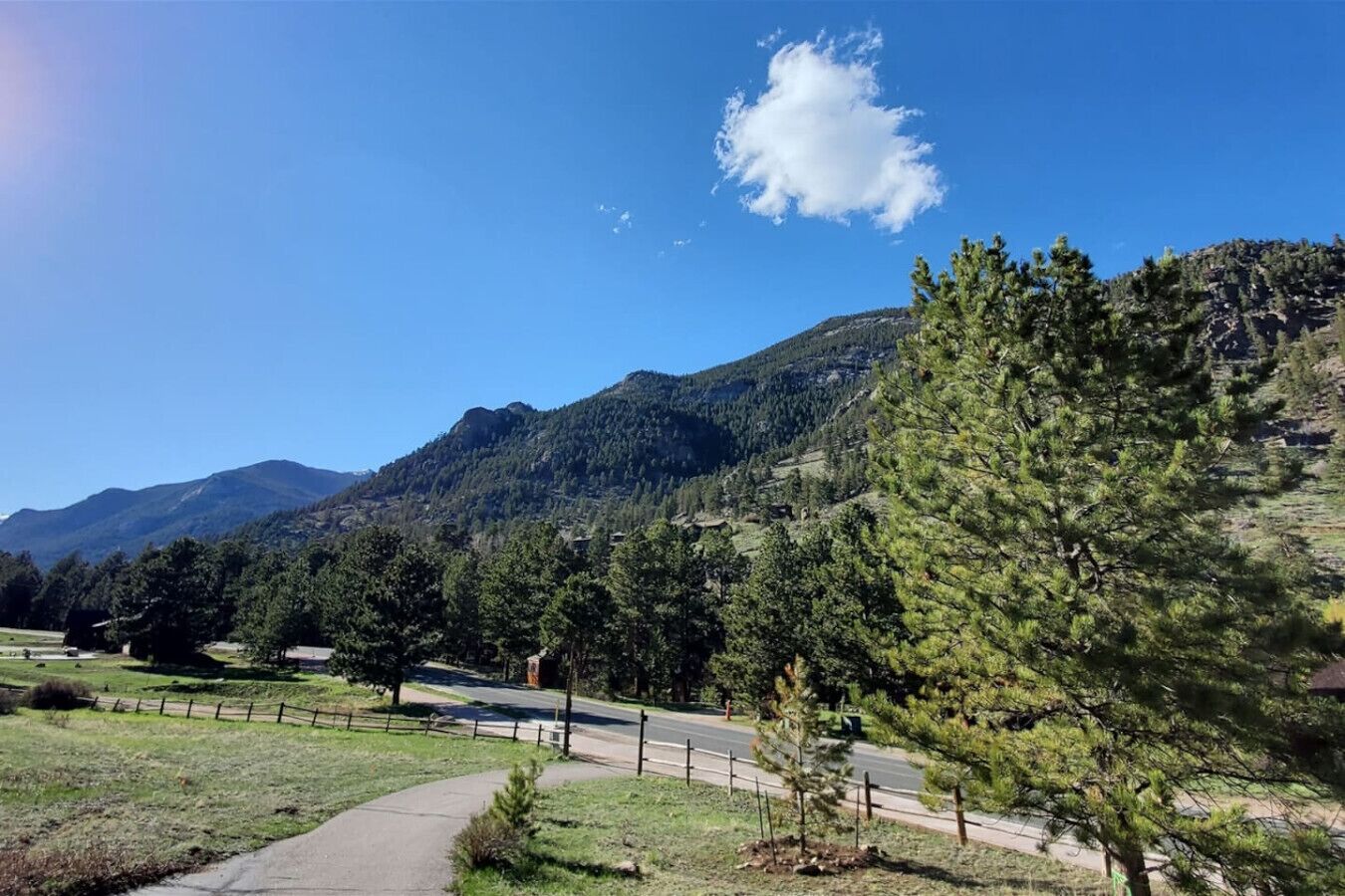 Un paisaje montañoso con cielo despejado, un camino pavimentado y una cerca.