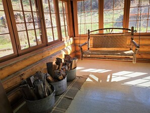 A log cabin interior with a wooden bench, large windows, and metal buckets of firewood. - Wranglers Cabin- Close to RMNP Entrance less than 4 minutes away! (Estes Park)
