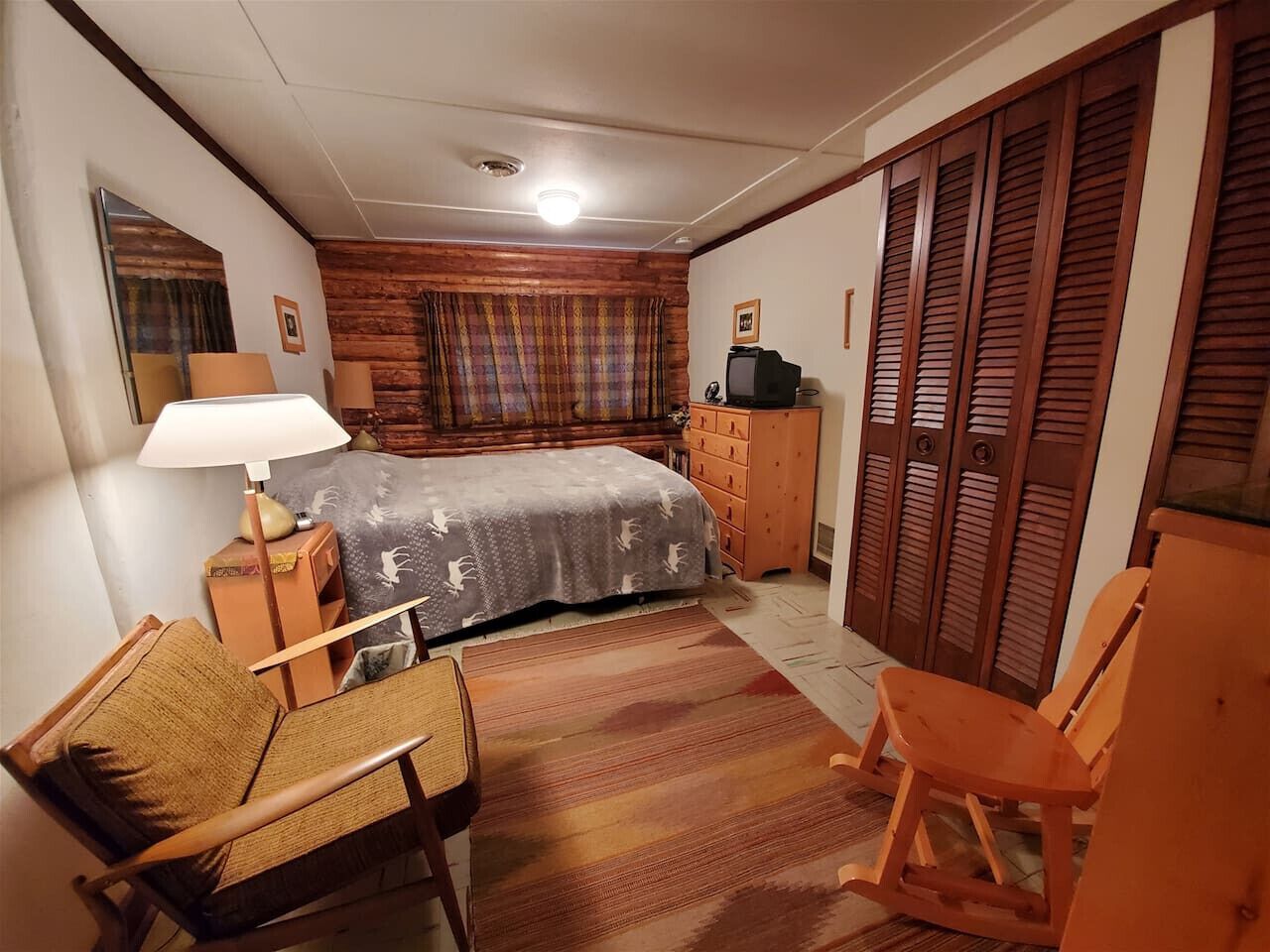 A bedroom with a bed, wooden wardrobe, a desk with a lamp, and a chair.