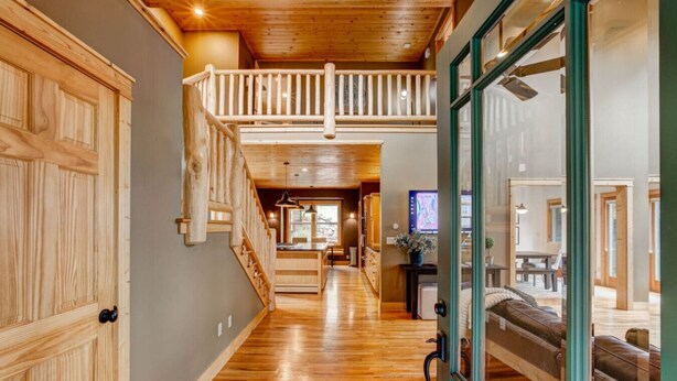 A wooden interior with a staircase, a dining area, and a view through a glass door.