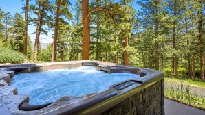 A hot tub in a forested area with a stone wall and a wooden roof.