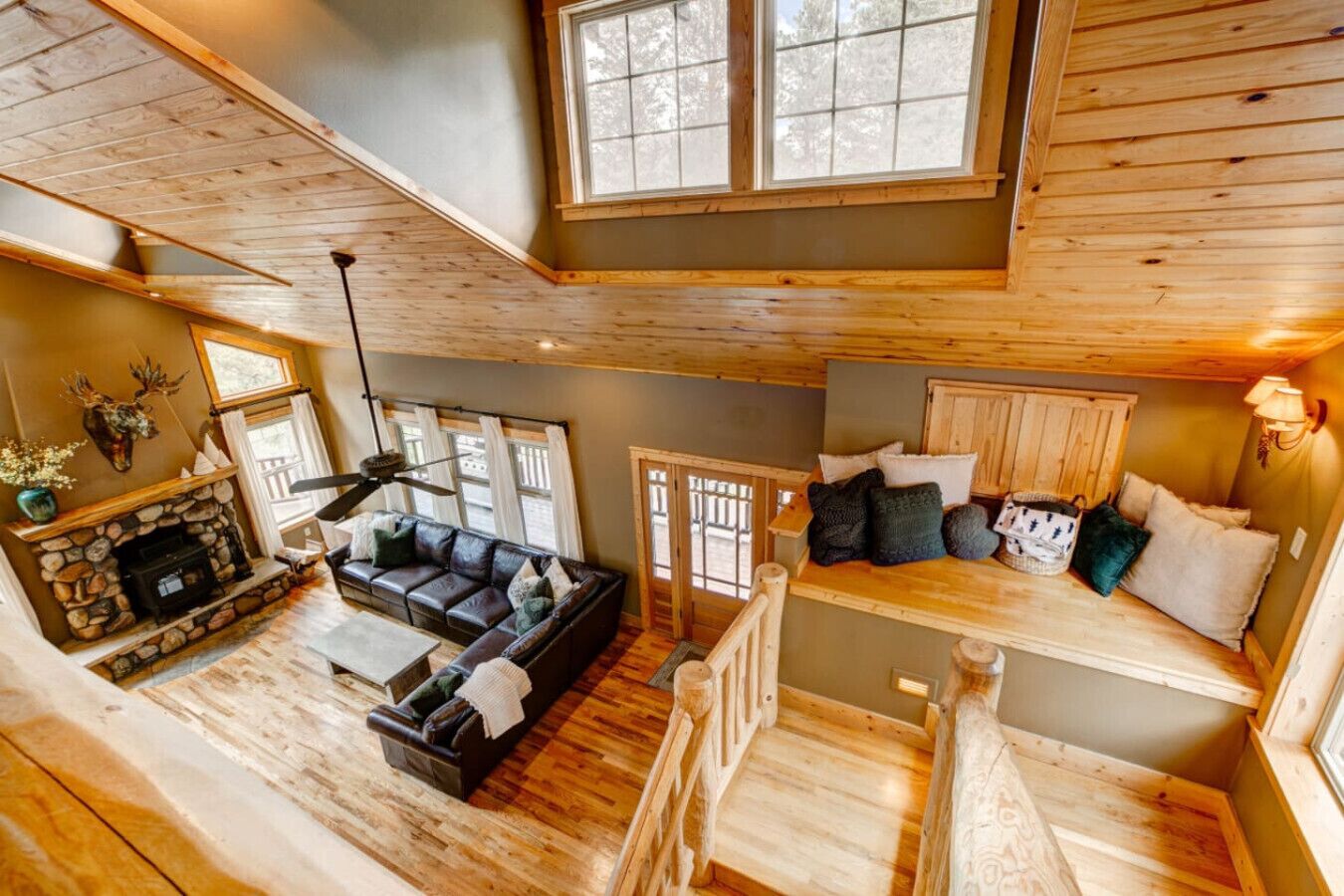 A multi-level cabin with a stone fireplace, a leather sofa, and a wooden staircase.