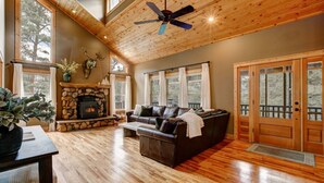 A spacious living room with a stone fireplace, leather sofa, and large windows.