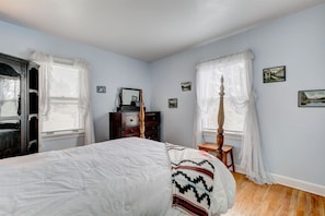 Une chambre à coucher avec un lit, une commode, un miroir et une fenêtre avec des rideaux.