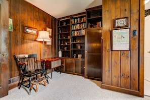 Une pièce avec des boiseries, un bureau avec une lampe, une chaise, une bibliothèque et un meuble.
