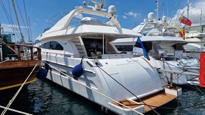 Ein Yachthafen mit mehreren vor Anker liegenden Yachten, darunter eine weiße Yacht namens "Blue Ocean" mit überdectem Deckbereich und einem Holldeck an der Heck.