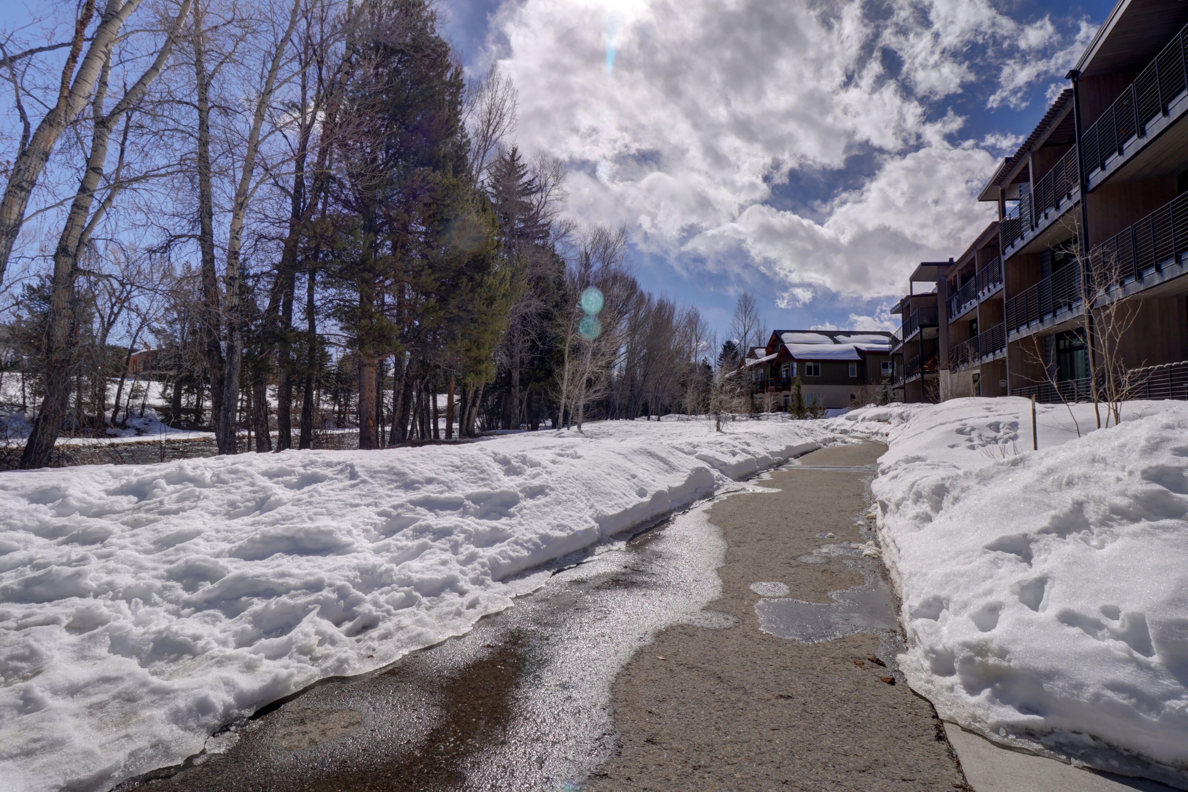 A snow-covered pathway leading to a building with multiple balconies and a clear sky.