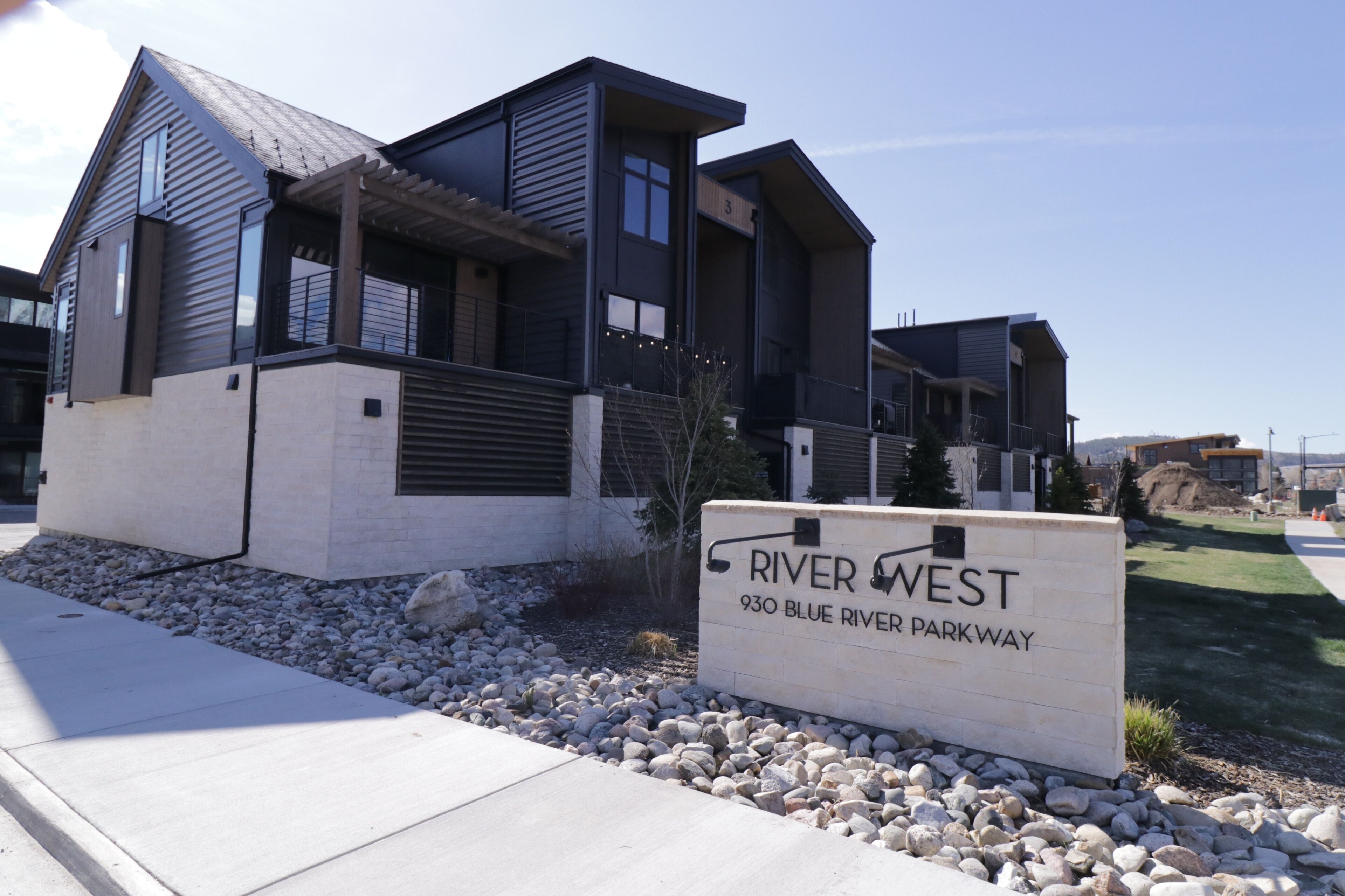 Una casa moderna de dos pisos con un cartel que indica 'River West 930 Blue River Parkway'.