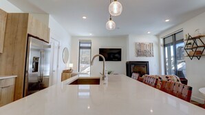 A modern kitchen with a large island, stainless steel appliances, pendant lighting, and a cozy seating area with a fireplace. - River West 515 2 Bedroom Condo (Silverthorne)