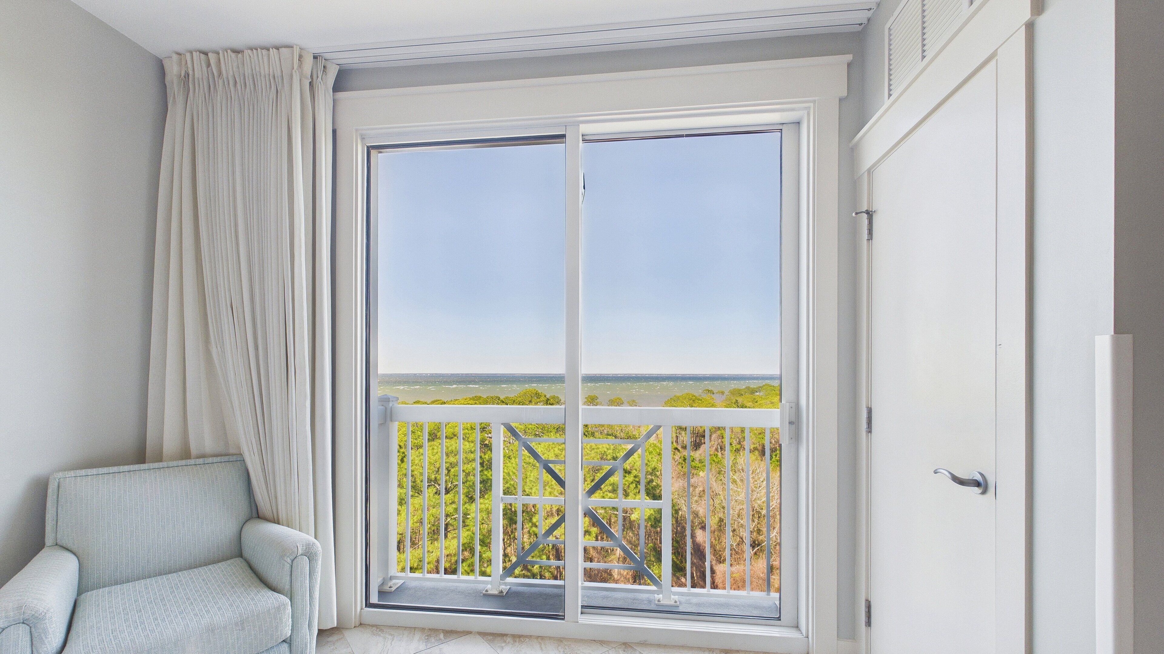 Une pièce dotée d’une grande porte-fenêtre coulissante donnant sur un balcon avec vue sur la verdure et une côte lointaine.