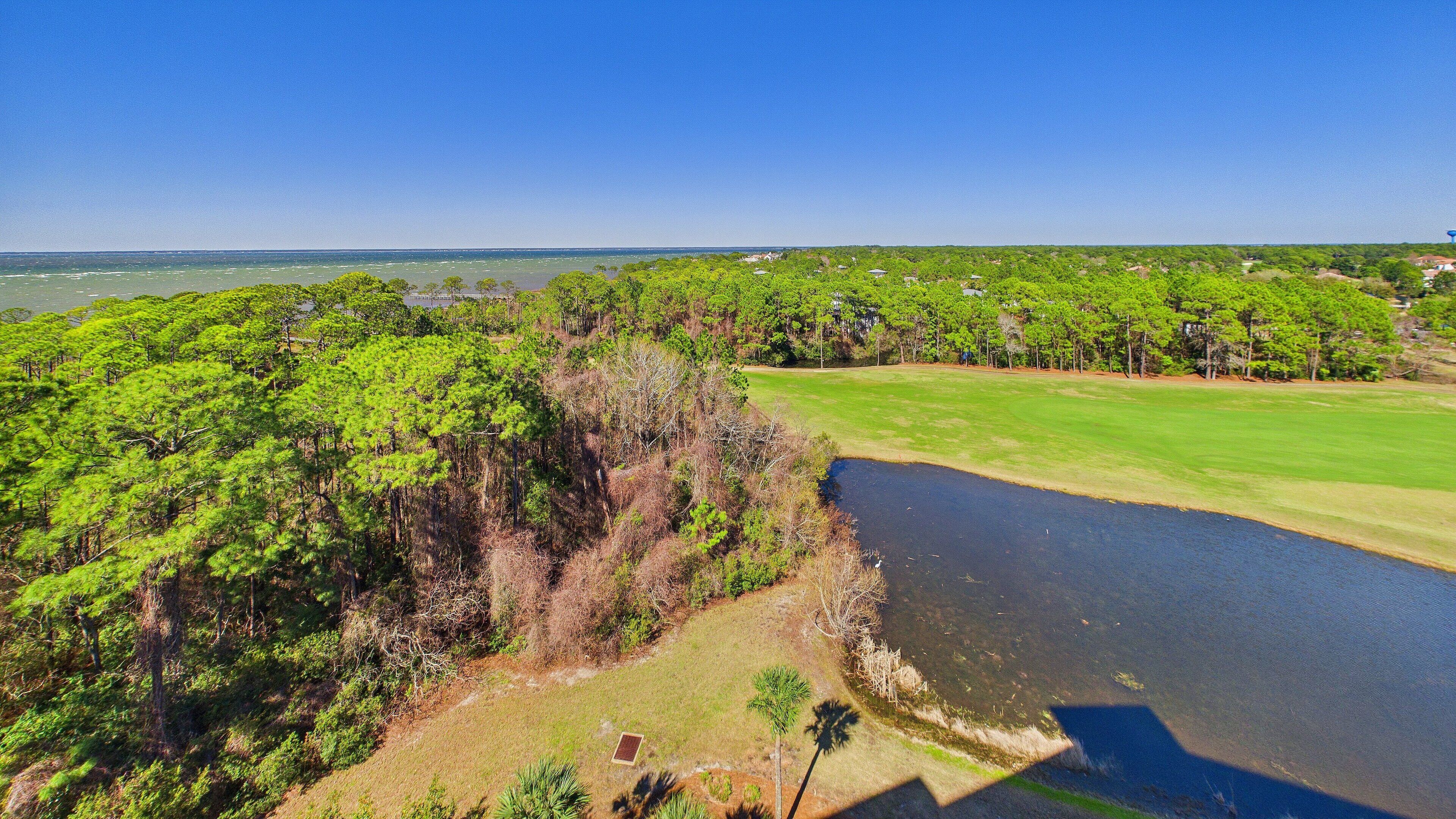 Un campo de golf con un estanque, rodeado de vegetación exuberante y un cielo azul despejado.