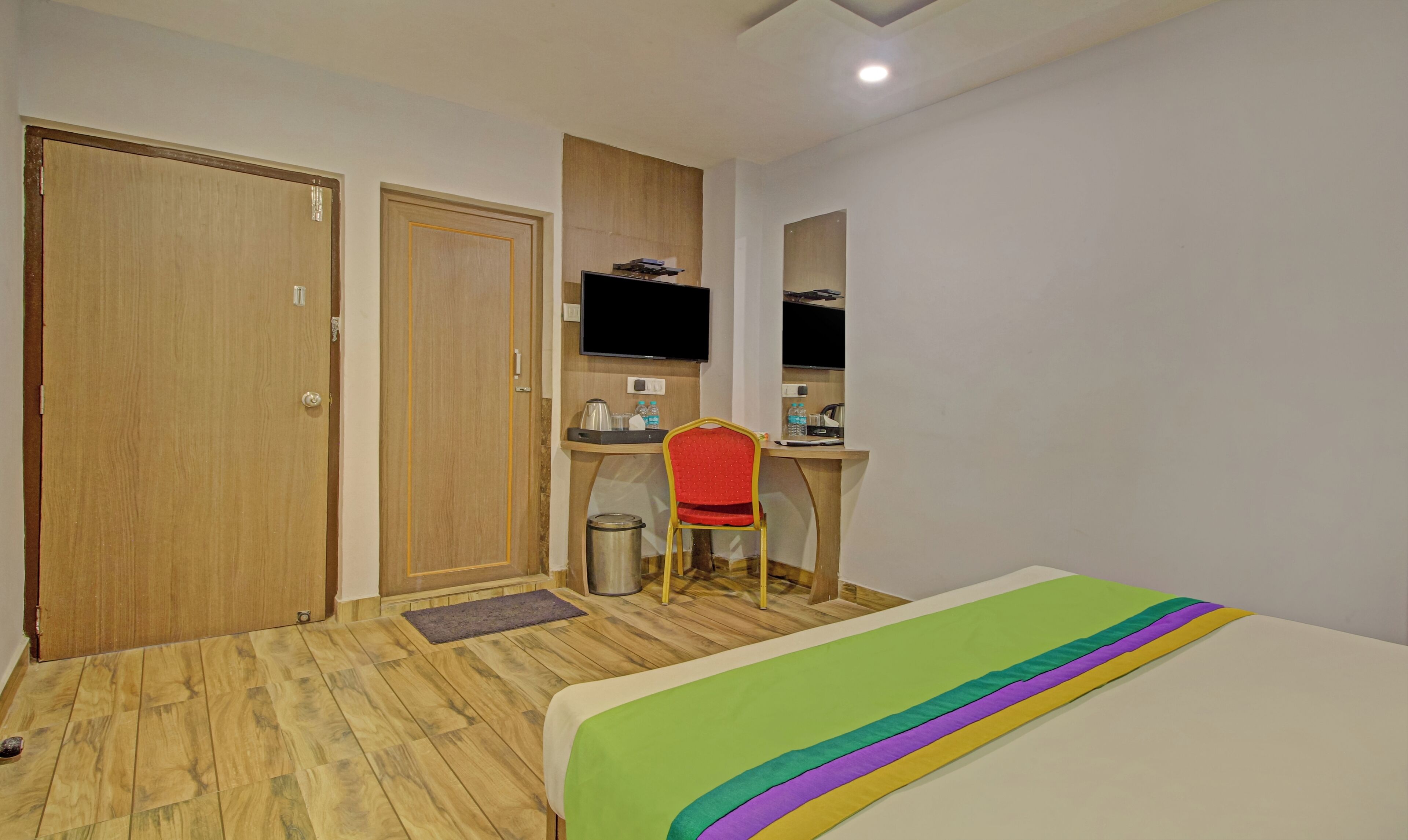 Une chambre d’hôtel avec un plancher en bois, un lit recouvert d’une courtepointe aux couleurs de l’arc-en-ciel, un bureau avec une chaise, une télévision et une poubelle.