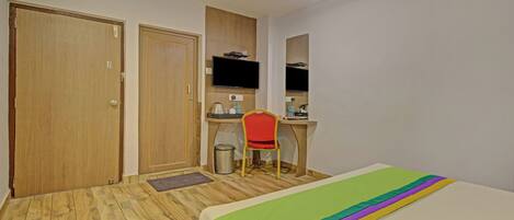 Une chambre d’hôtel avec un plancher en bois, un lit recouvert d’une courtepointe aux couleurs de l’arc-en-ciel, un bureau avec une chaise, une télévision et une poubelle.