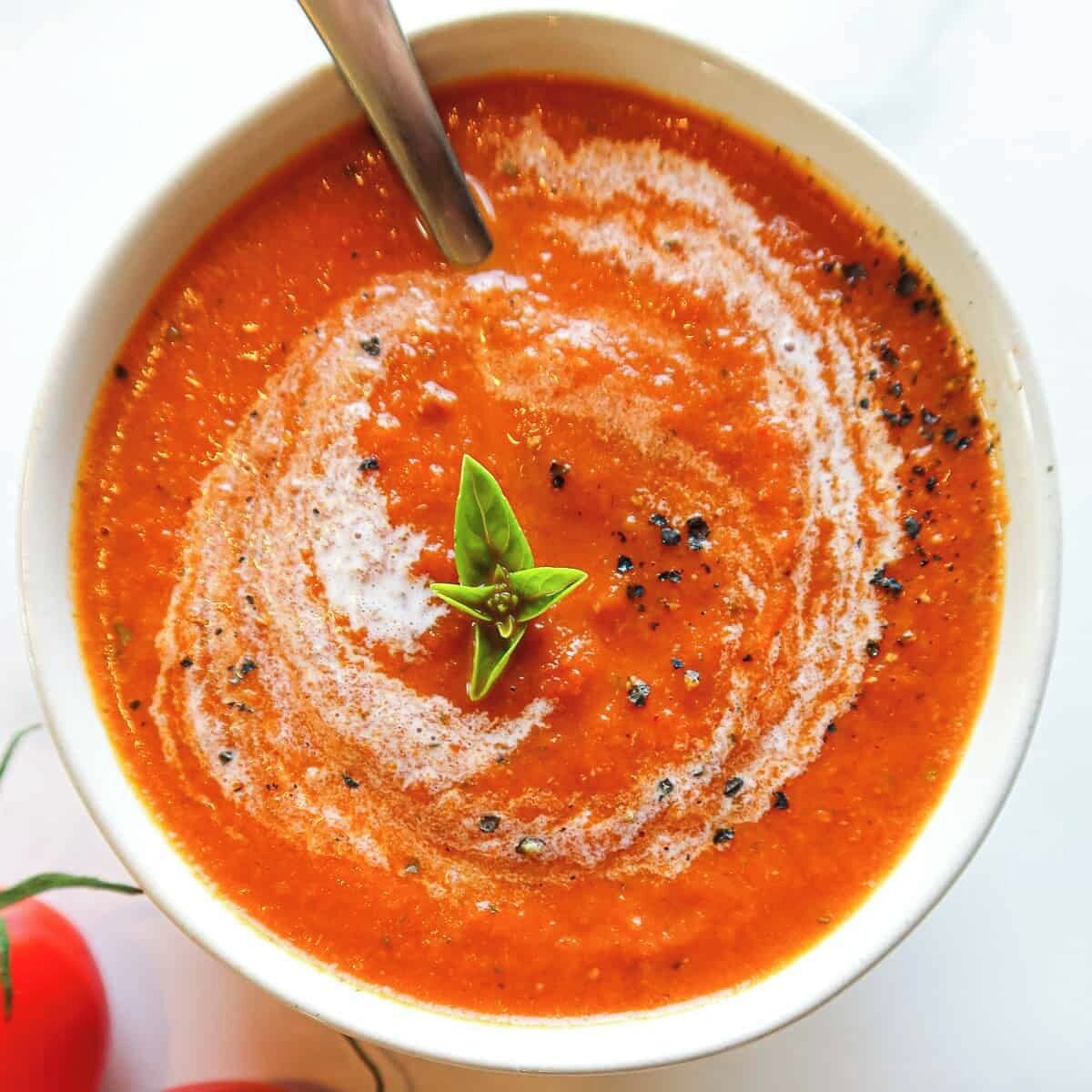 Una ciotola di zuppa di pomodoro guarnita con una foglia di basilico e pepe nero.
