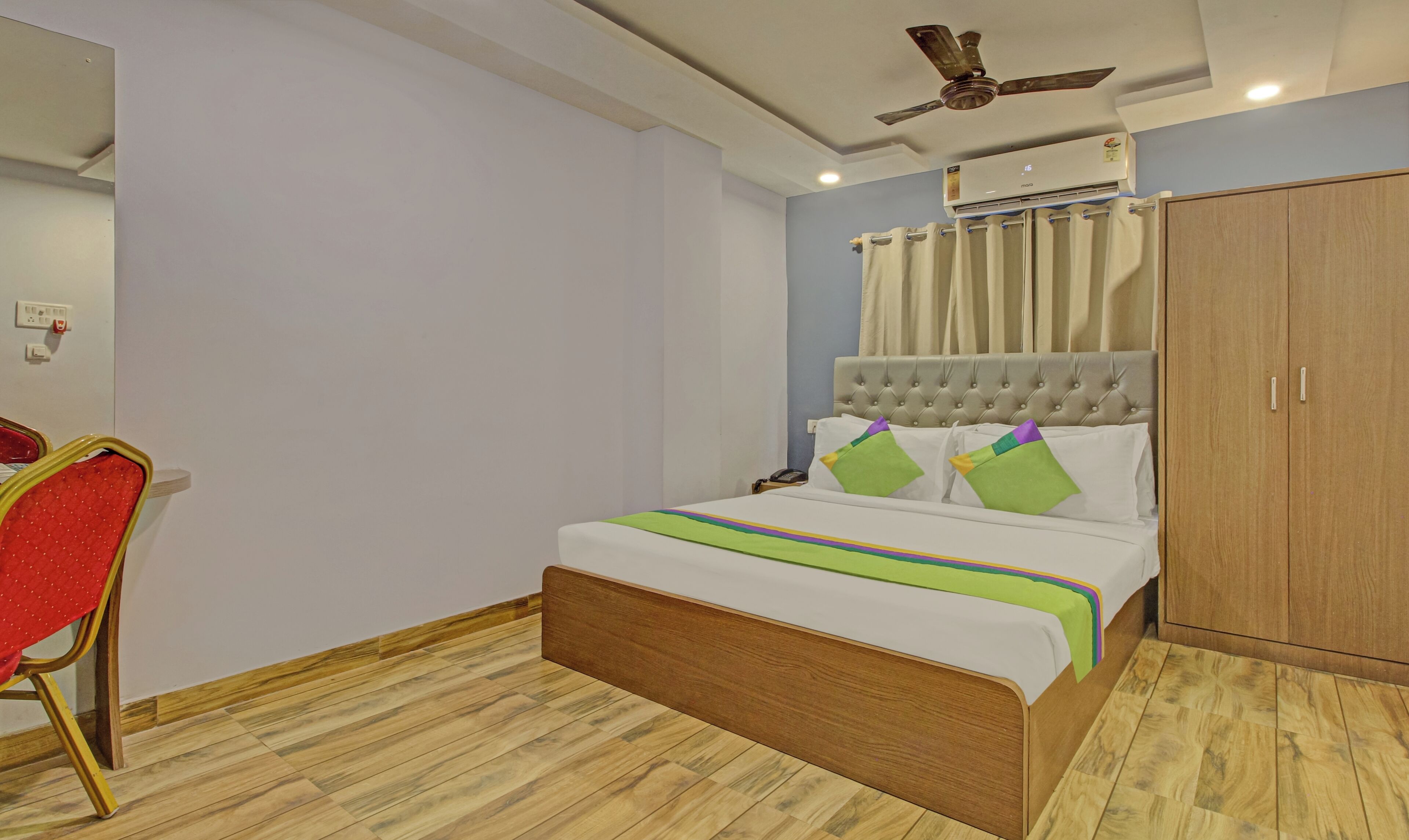 Quarto com cama, ventoinha no teto, ar condicionado, guarda-roupa e uma cadeira.