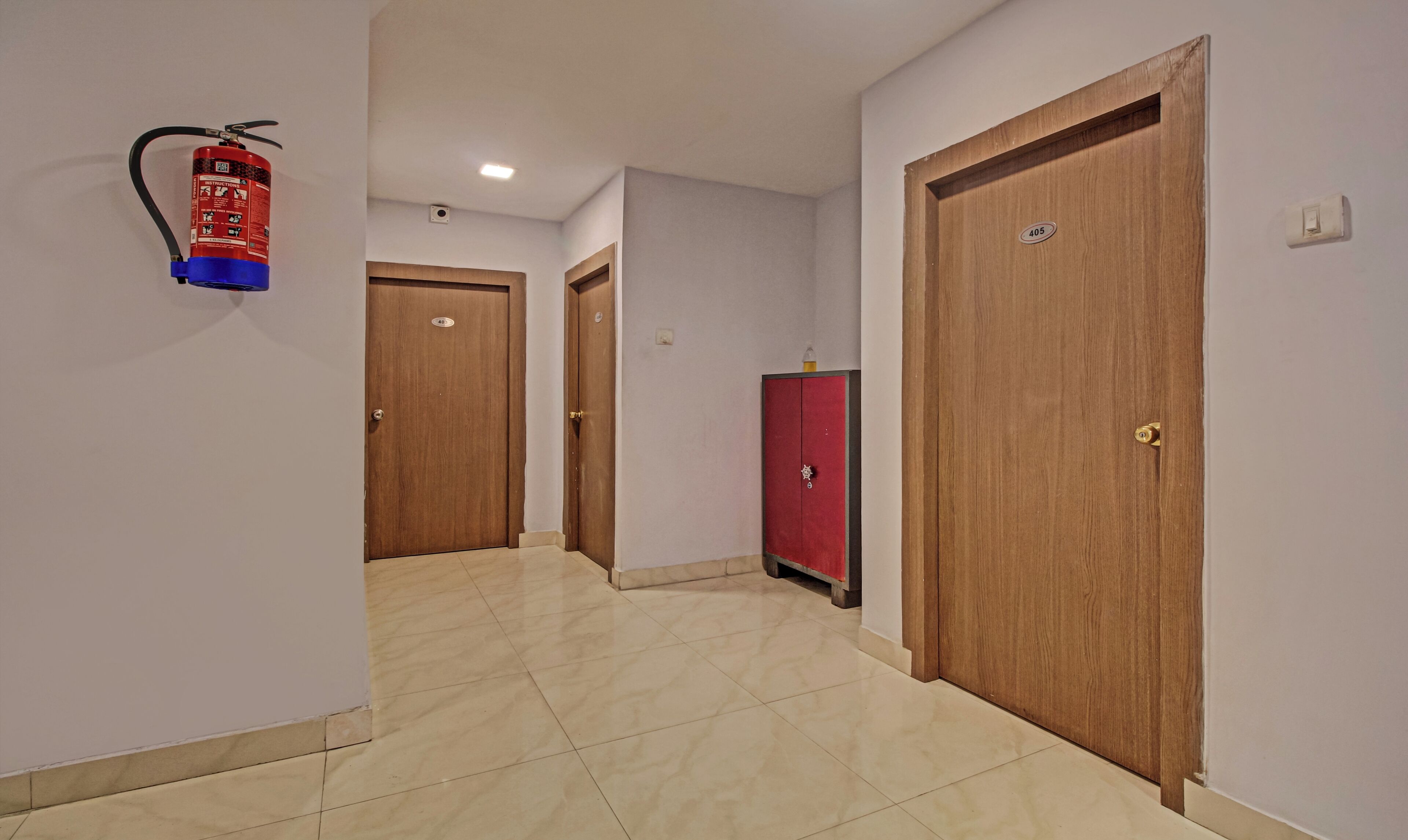 Um corredor com três portas de madeira, um armário vermelho e um extintor fixado na parede.