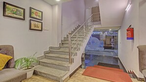 Una escalera con barandillas metálicas, un extintor de incendios en la pared y una planta en el rellano.