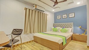 Un dormitorio con cama, una silla, un escritorio, aire acondicionado, ventilador de techo y una mesita de noche con lámpara.