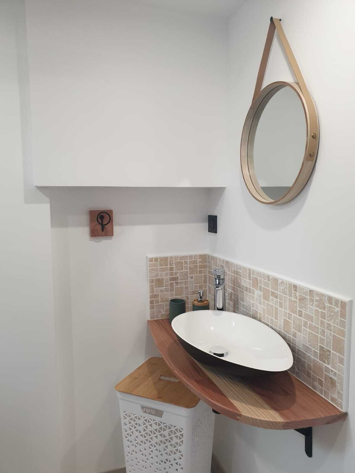 Een badkamer met een witte wastafel, een houten aanrechtblad en een ronde spiegel.