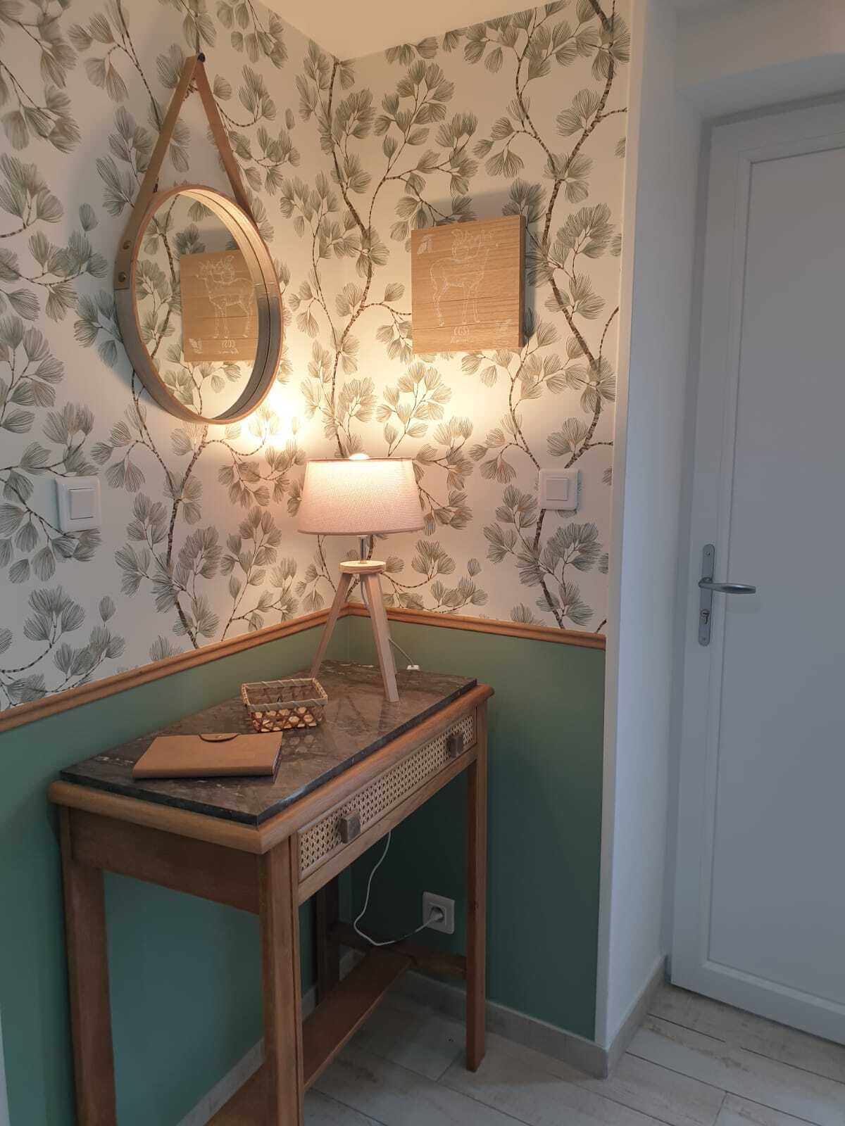 Quarto de canto com mesa de consola de madeira, espelho pendurado, luminária na parede e uma porta.