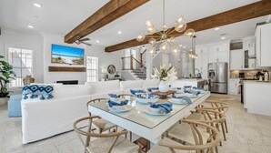 Une cuisine moderne avec des meubles blancs, un îlot central et un coin repas comprenant une table en verre et des chaises en bois.