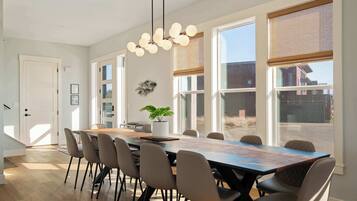 A spacious dining area with a long table, multiple chairs, and a hanging light fixture.