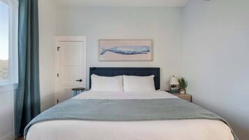 A bedroom with a bed, a nightstand, a wall-mounted air conditioner, a door, and a window with curtains.