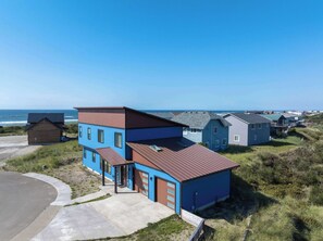 A coastal residential area with modern houses, a clear view of the ocean, and a paved driveway leading to a house with a garage.