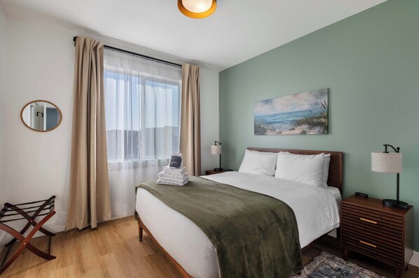 A neatly arranged bedroom with a bed, bedside table, lamp, and a painting on the wall.