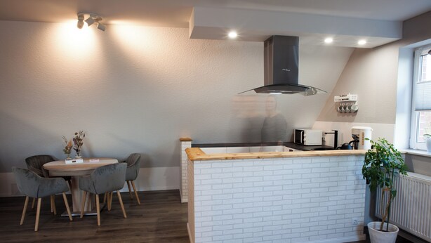 A modern kitchen with a white brick backsplash, wooden countertop, and a built-in island. There is a dining area with a round table and chairs. - Cozy vacation apartment in East Frisia - families & dogs welcome! (Hinte)