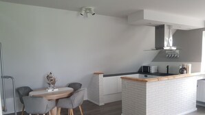A modern kitchen with a central island, grey chairs, a dining table, and a white brick backsplash. - Cozy vacation apartment in East Frisia - families & dogs welcome! (Hinte)