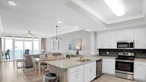 Una cocina moderna con armarios blancos, encimera de granito, electrodomésticos de acero inoxidable y un comedor con candelabro.