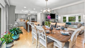 A modern kitchen with white cabinets, a dining area with a wooden table, and a living room with a sofa.