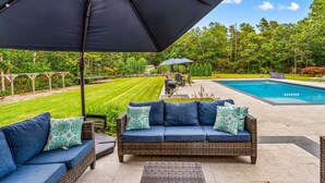 A patio with a wicker sofa, an umbrella, and a pool.