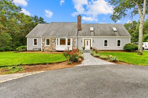 A two-story house with a stone facade, a front porch, and a well-maintained lawn. - New listing 4bd w/ heated pool, chicken coop, kids playground, wifi (Sandwich)
