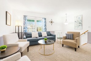 Una sala de estar con un sofá gris, un sillón beige, una mesa de centro redonda y una lámpara.
