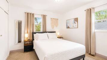 A bedroom with a bed, bedside tables, a wall-mounted artwork, and a window with curtains.