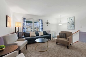 A living room with a sofa, armchairs, a coffee table, a lamp, and a painting.