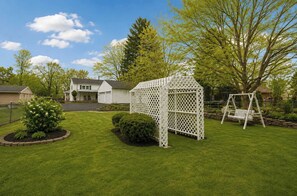Patio trasero residencial con un parque infantil blanco, un columpio y un césped bien cuidado.