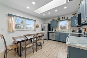 A modern kitchen with a dining area, featuring a wooden table and chairs, a refrigerator, and a sink.