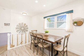 Un comedor con una mesa y sillas de madera, un reloj decorativo en la pared y un ventanal con vistas al agua.