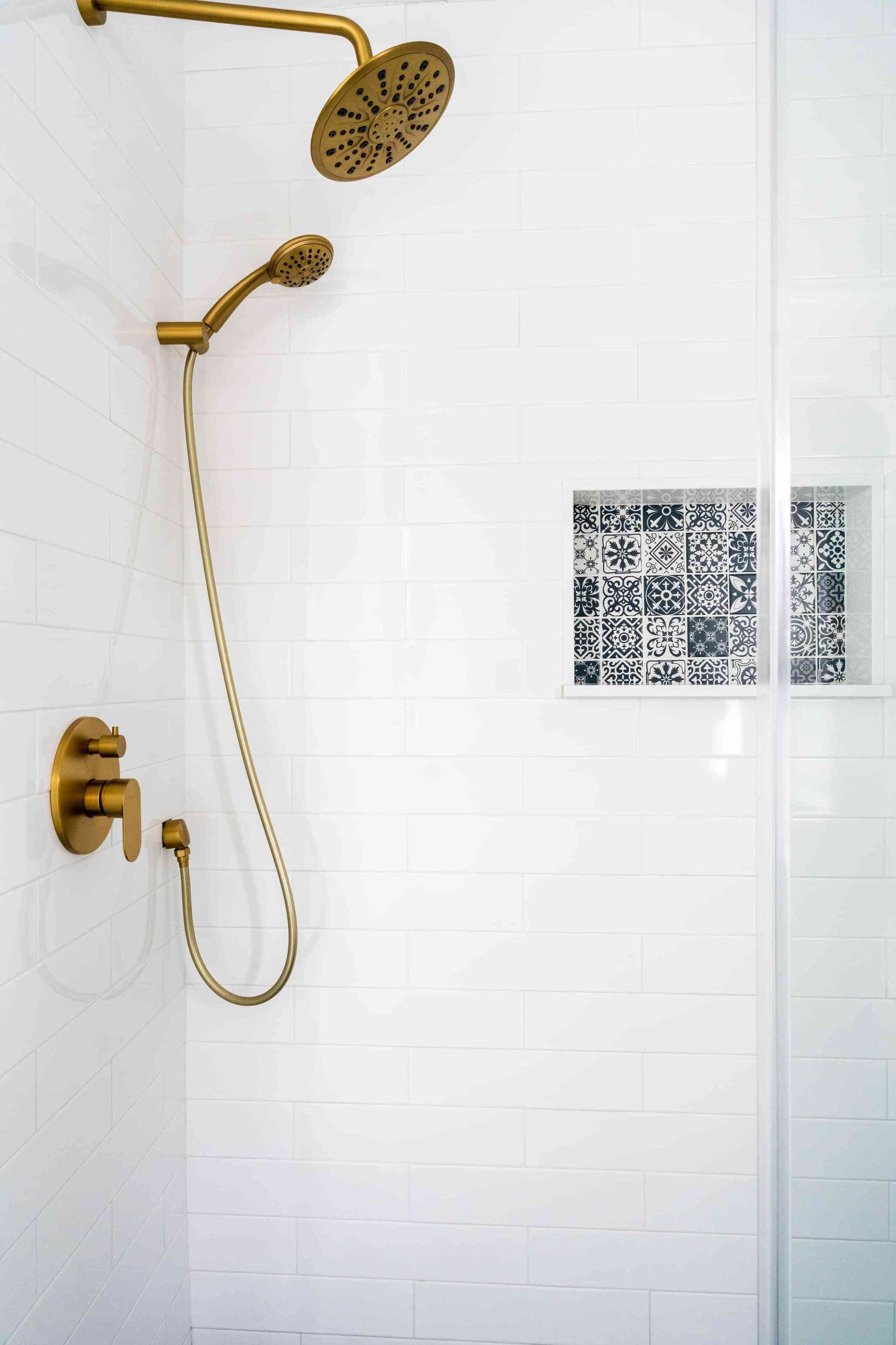 A shower with a gold fixture and a patterned tile wall.