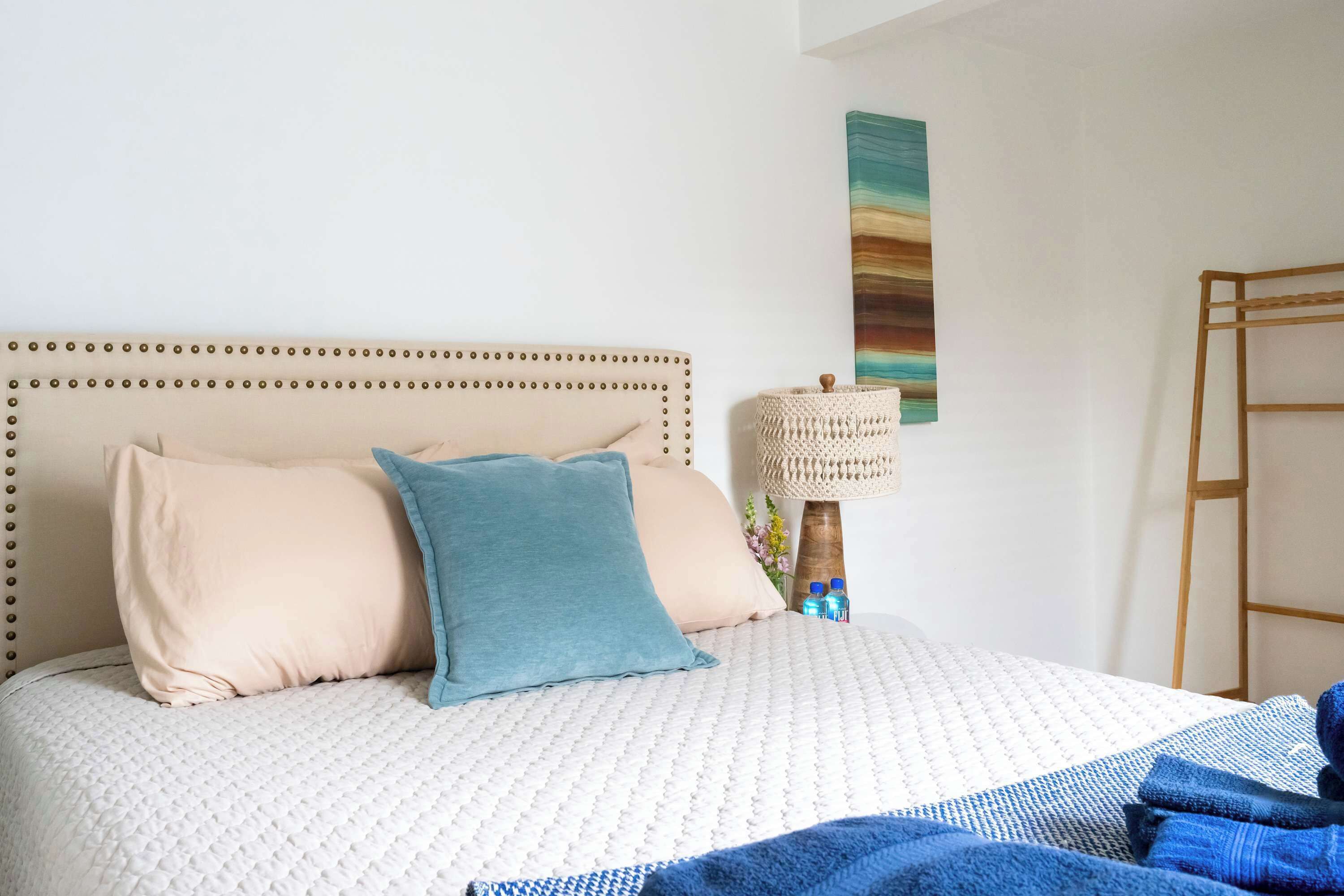 A neatly made bed with a headboard, a lamp, and a wall-mounted artwork.