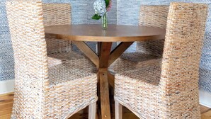 Un comedor con una mesa redonda de madera, dos sillas de mimbre, una lámpara colgante y un papel tapiz estampado.