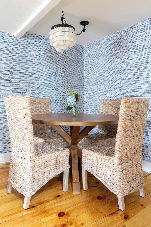 A dining area with a round wooden table, two wicker chairs, a hanging light fixture, and a patterned wall.