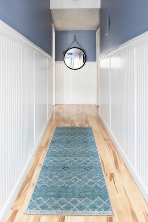 A hallway with a blue patterned rug, white wainscoting, and a round mirror on the wall. - Perfect for Large Groups, Downtown Newport 5 bed! (Newport)