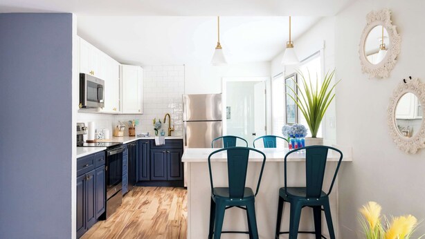 Una cocina con armarios blancos, un refrigerador de acero inoxidable y suelo de madera.