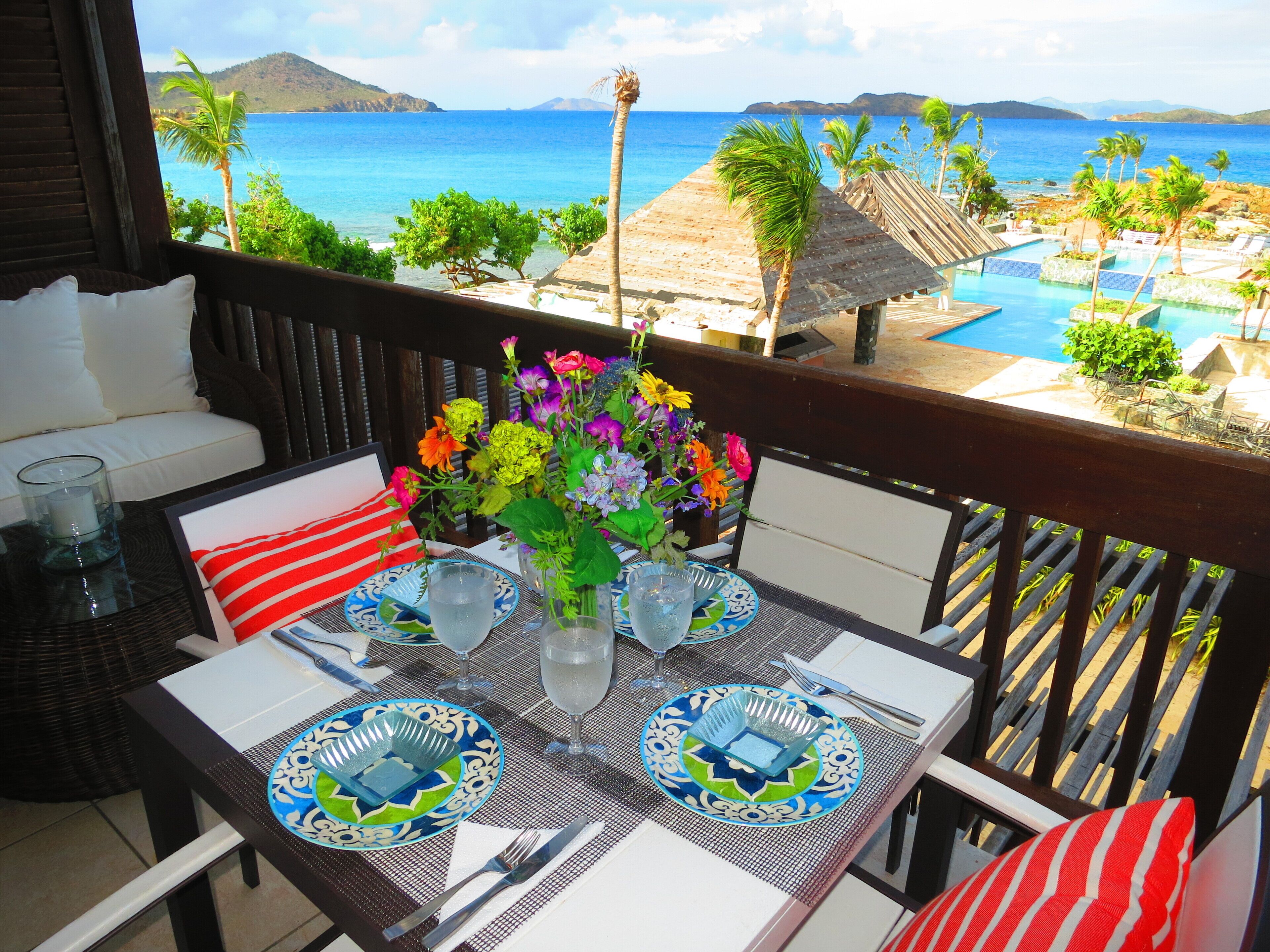 A dining area with a view of the ocean, a pool, and a beach.
